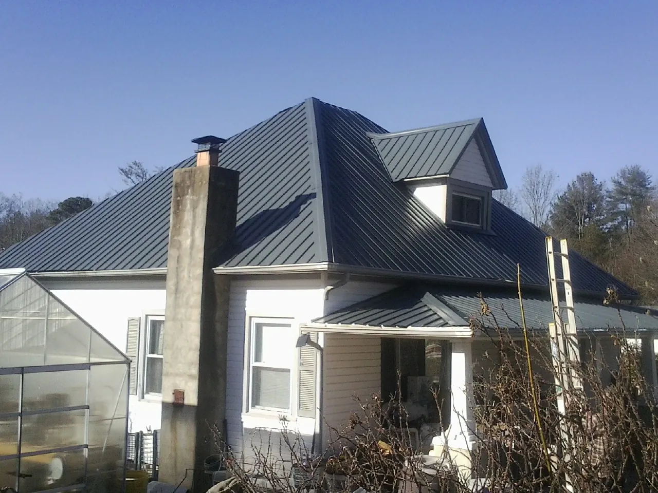 Dark blue standing seam metal roof on a white farmhouse with dormer — Slate & Tile Roof Repair by Roofing Brothers in Gardner