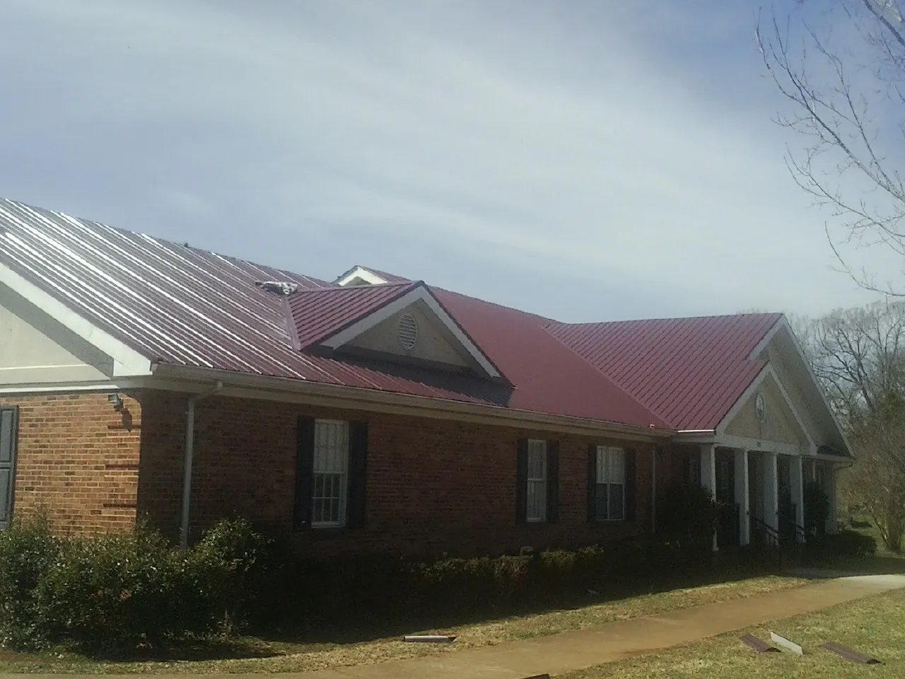 Red metal roof with gabled entries on a long brick building, from a Hail Damage Roof Repair job in Gardner