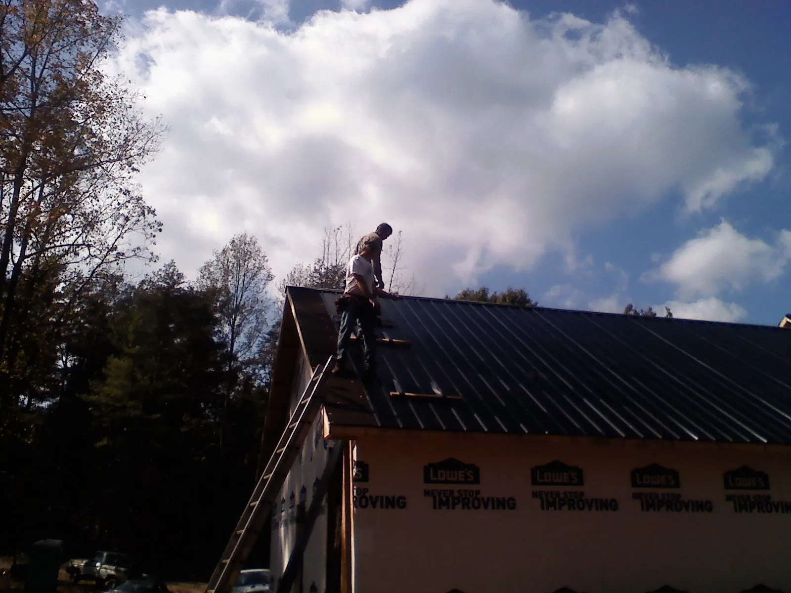 Roofer fastening dark metal panels high against a cloudy sky, from a Roof Inspection job in Gardner